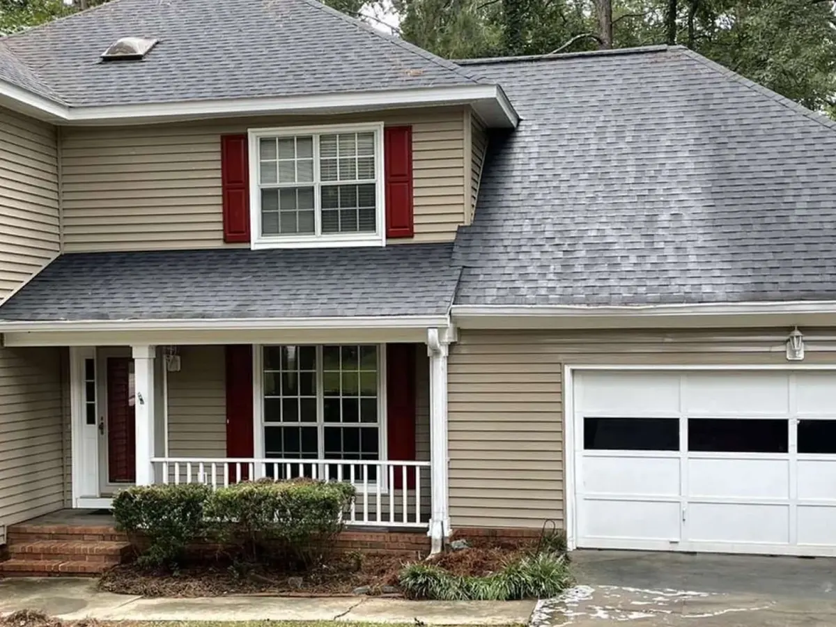Two-story home with tan siding and red shutters after the roof and gutters were cleared and washed