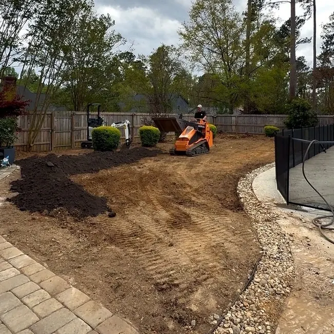 The same backyard before, bare red clay being graded with a skid steer